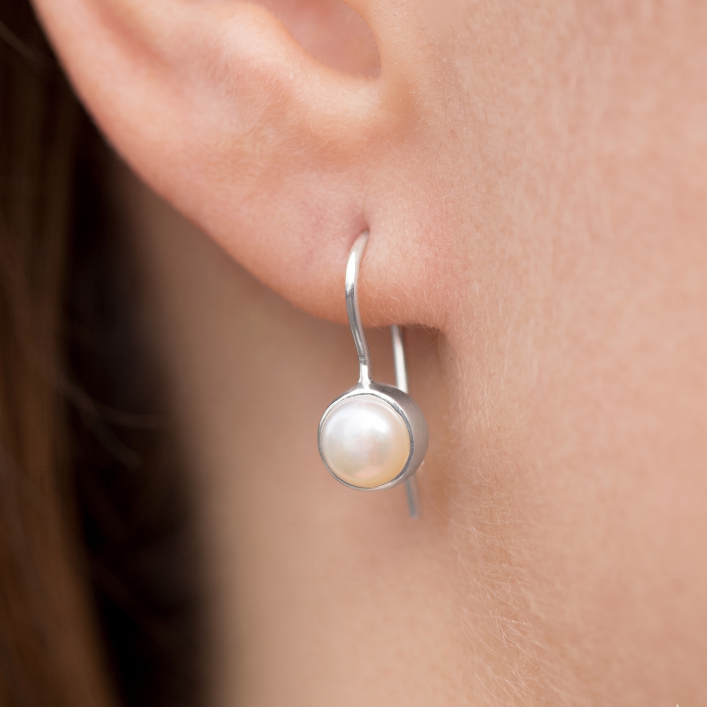 Silver earring with a pearl on an ear