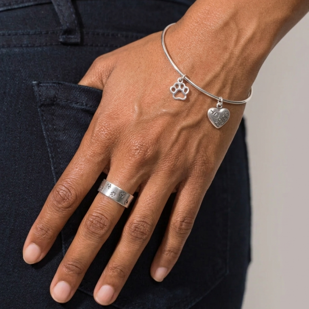 Hand wearing a silver ring and bracelet with paw and heart charms on a dark background