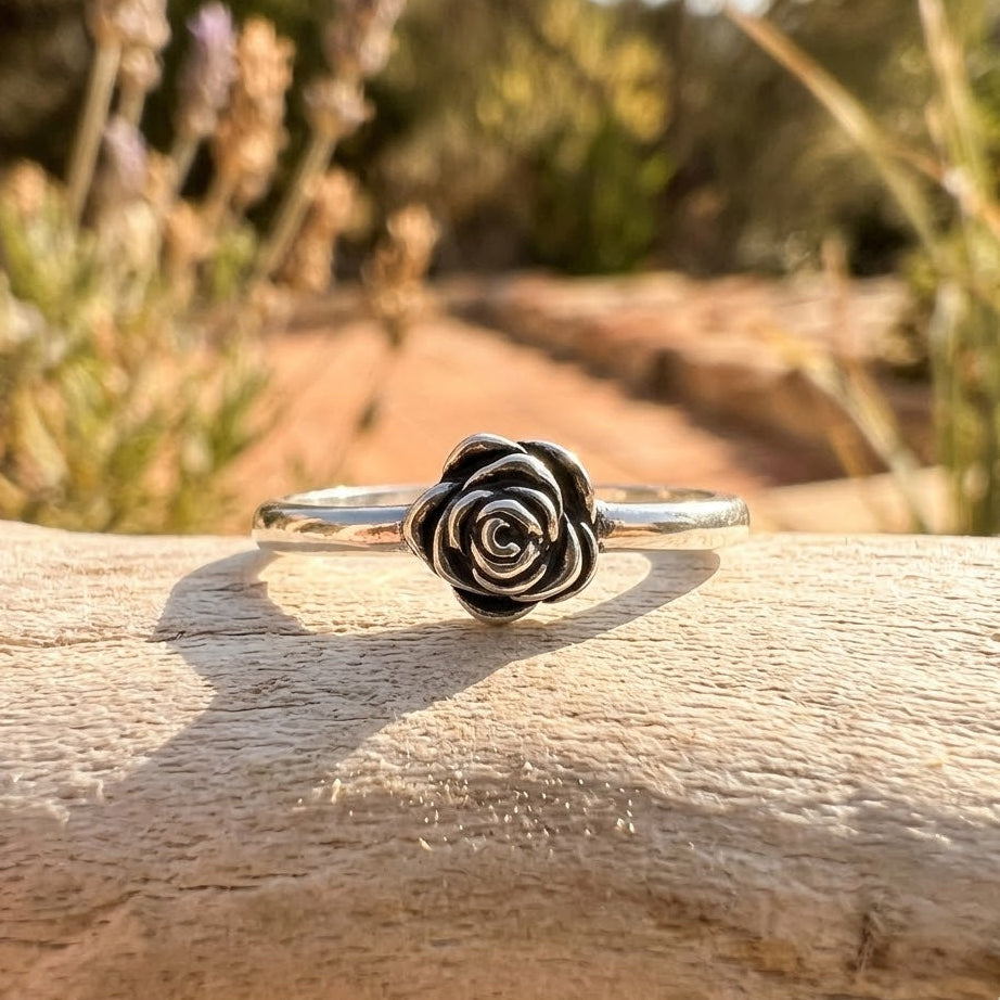 Silver rose-shaped ring on a wooden surface with blurred natural background