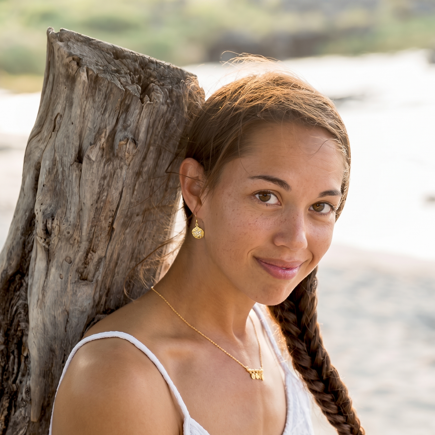 Woman with braided hair leaning against a wooden post by a body of water.