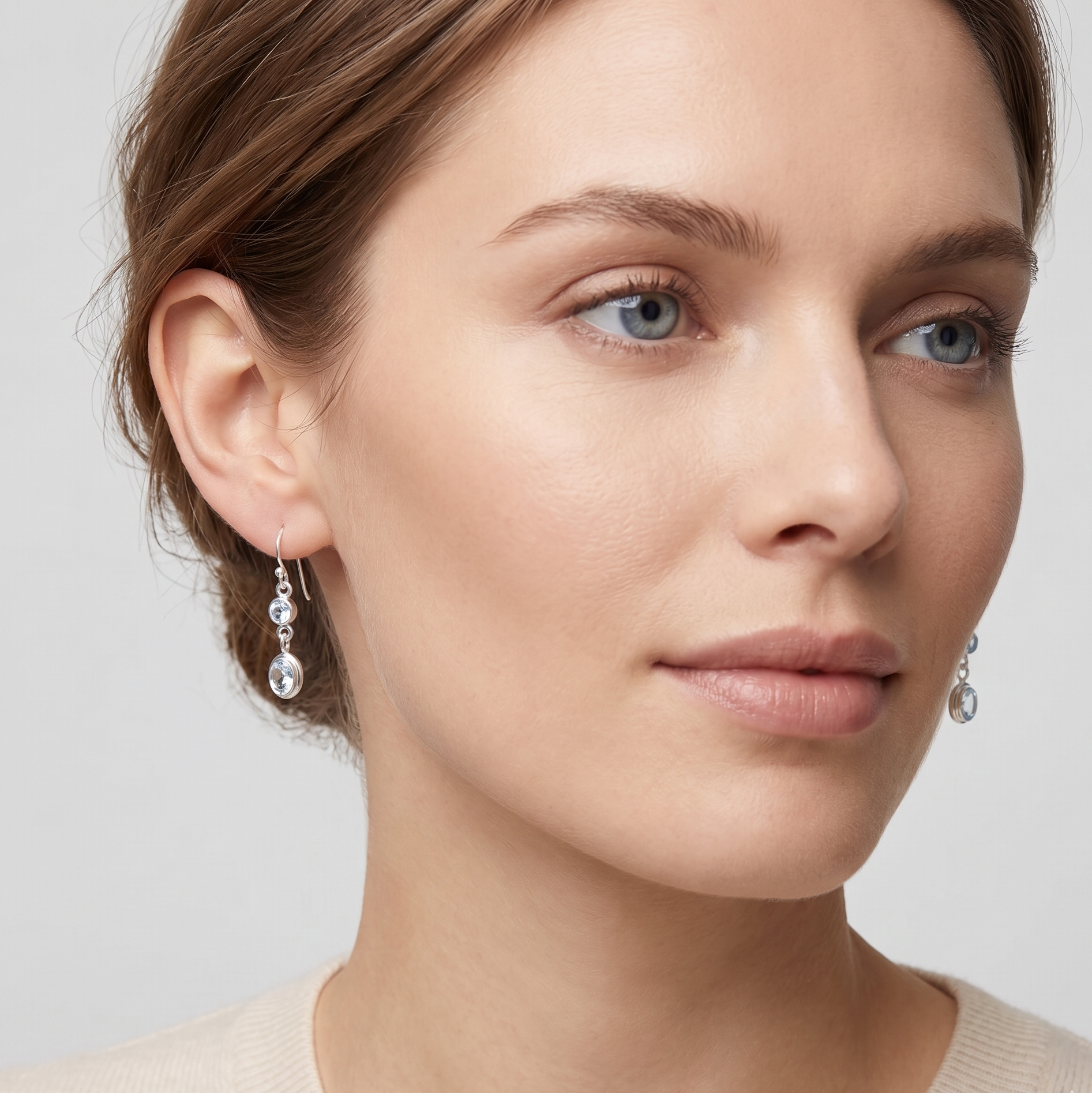 Close-up of a woman wearing silver earrings with a neutral background