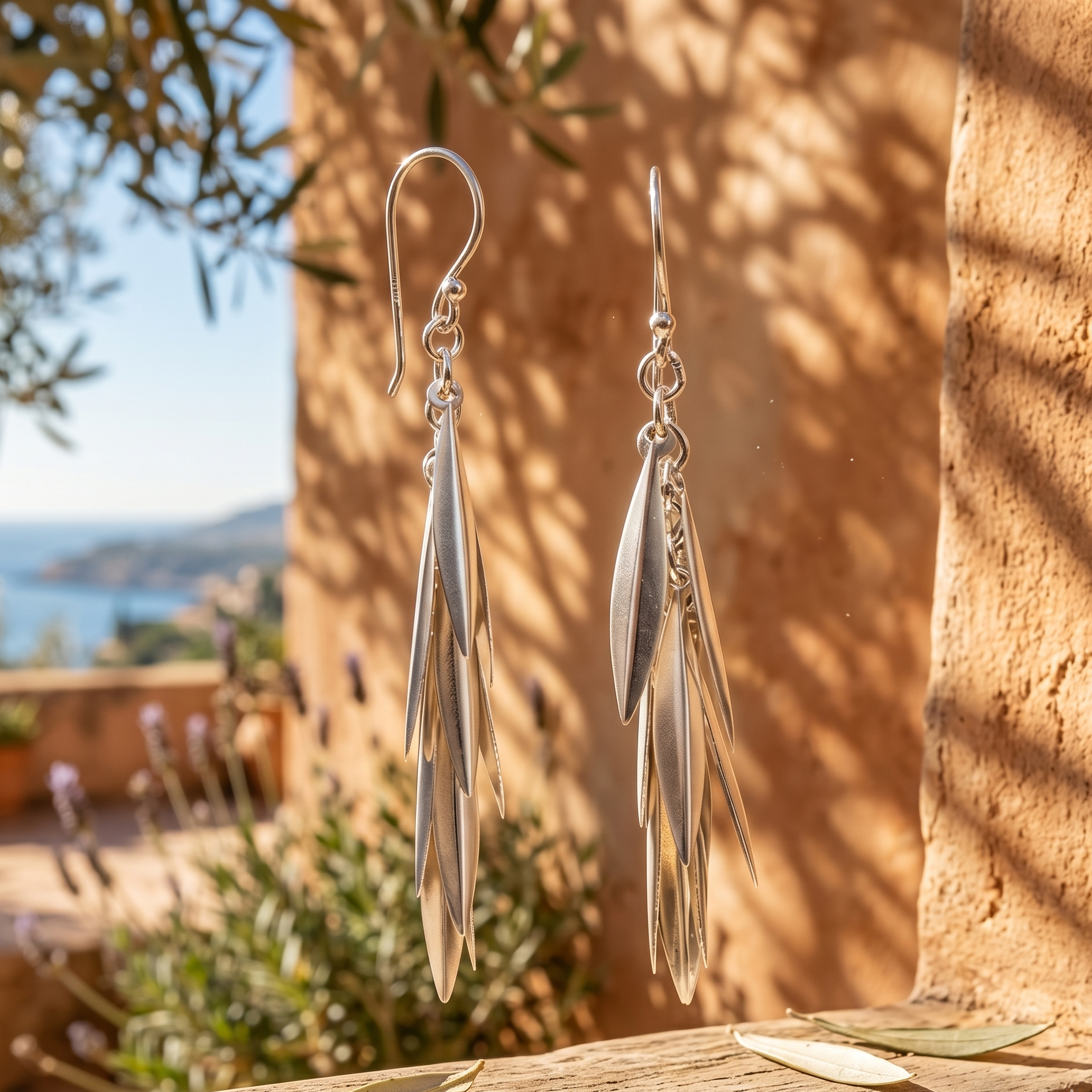 Silver leaf-shaped earrings on a wooden surface with a scenic background