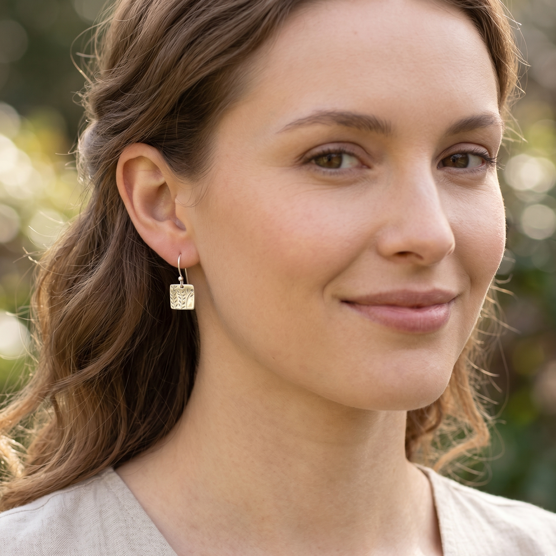 Woman wearing gold earrings with a blurred natural background