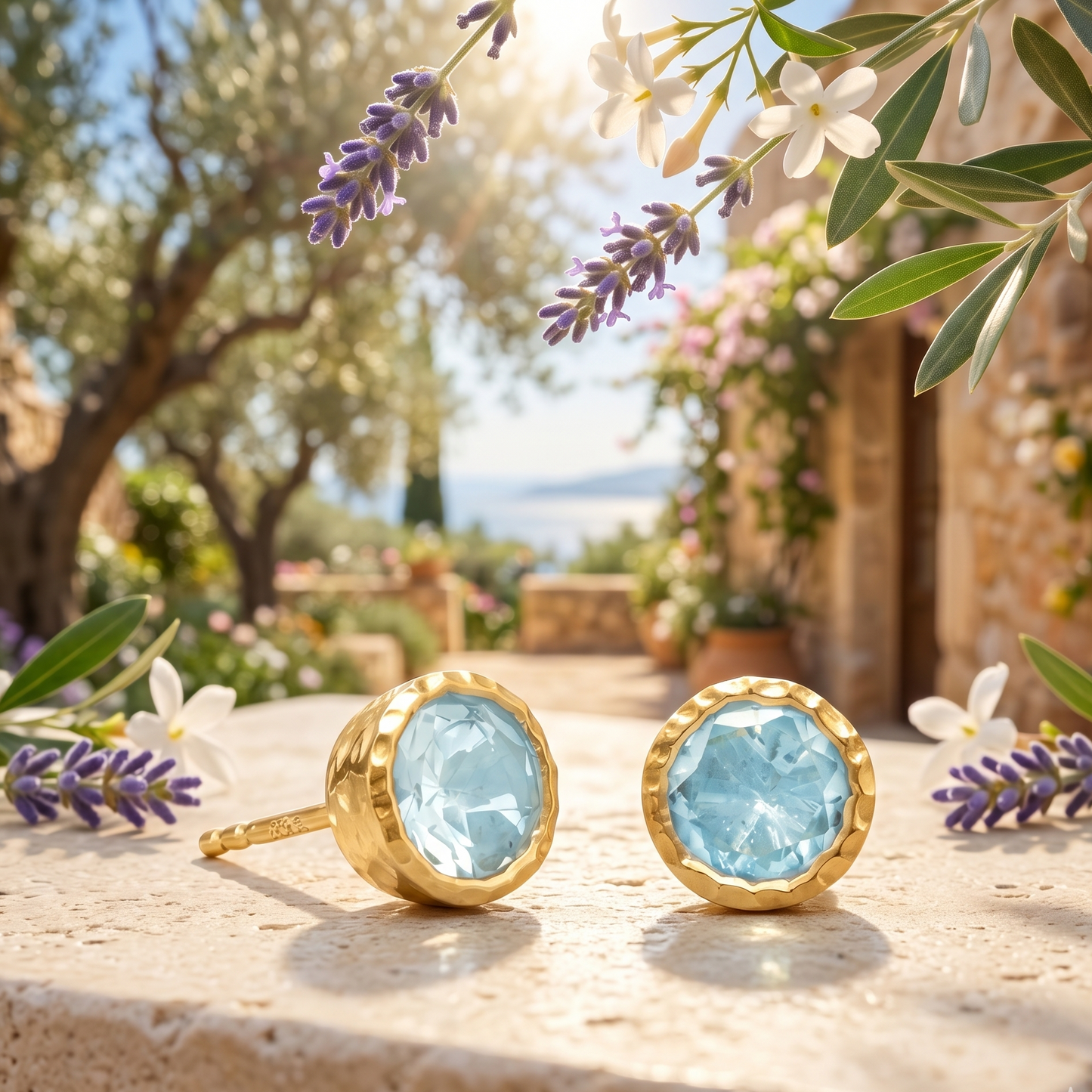 Gold earrings with blue gemstones on a stone surface with flowers and trees in the background