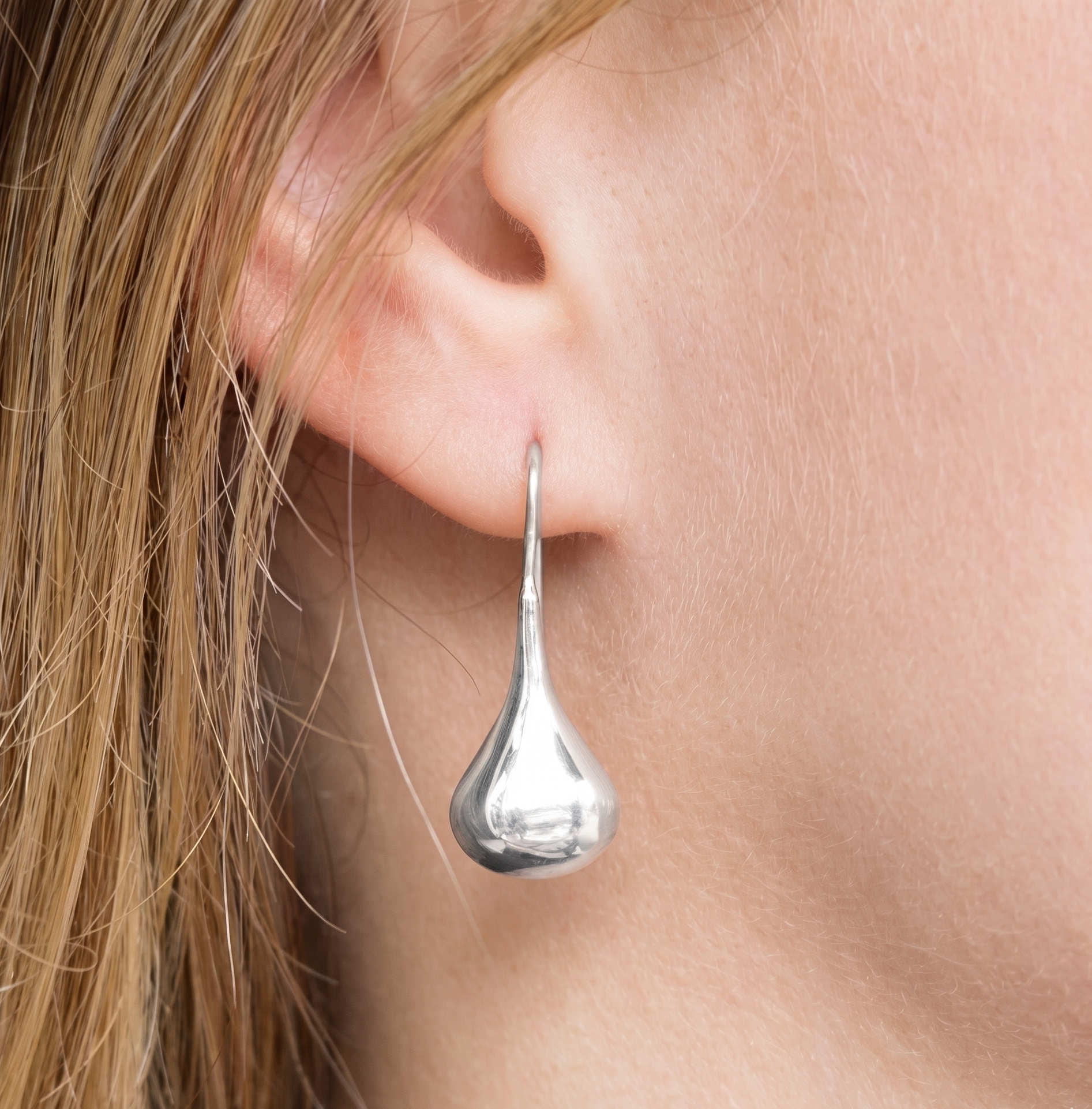 Silver teardrop earring worn by a person with blonde hair.