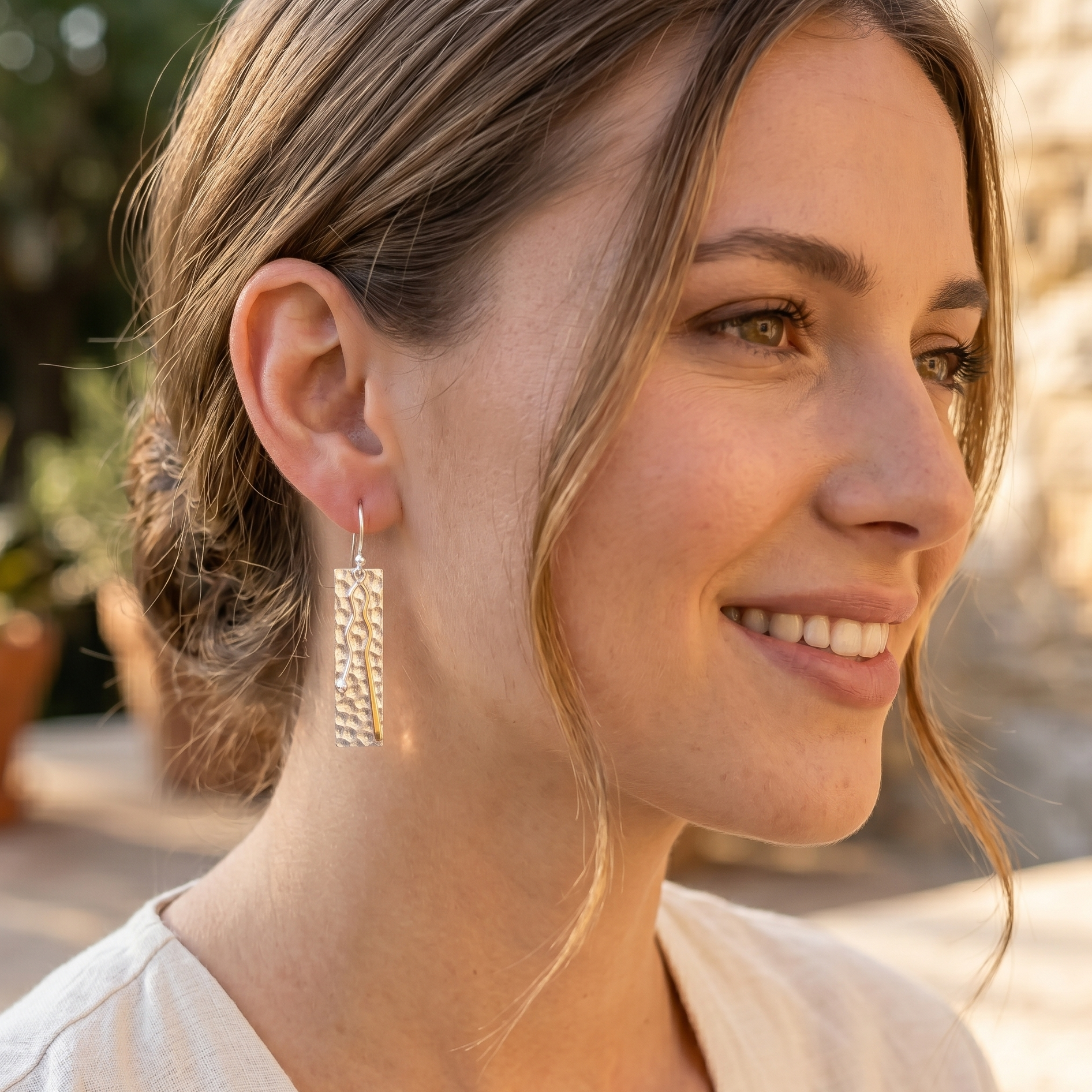Woman wearing gold earrings outdoors with a blurred background