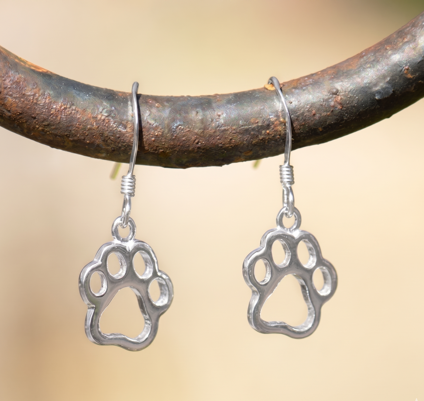 Silver paw print earrings hanging on a branch with a blurred background