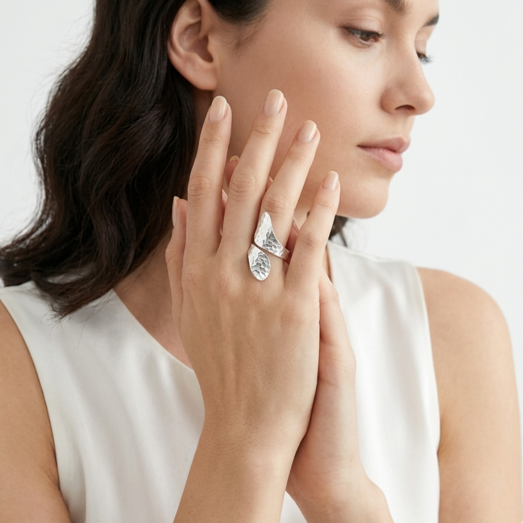 Woman wearing a silver ring with a pear-shaped gemstone on a plain background