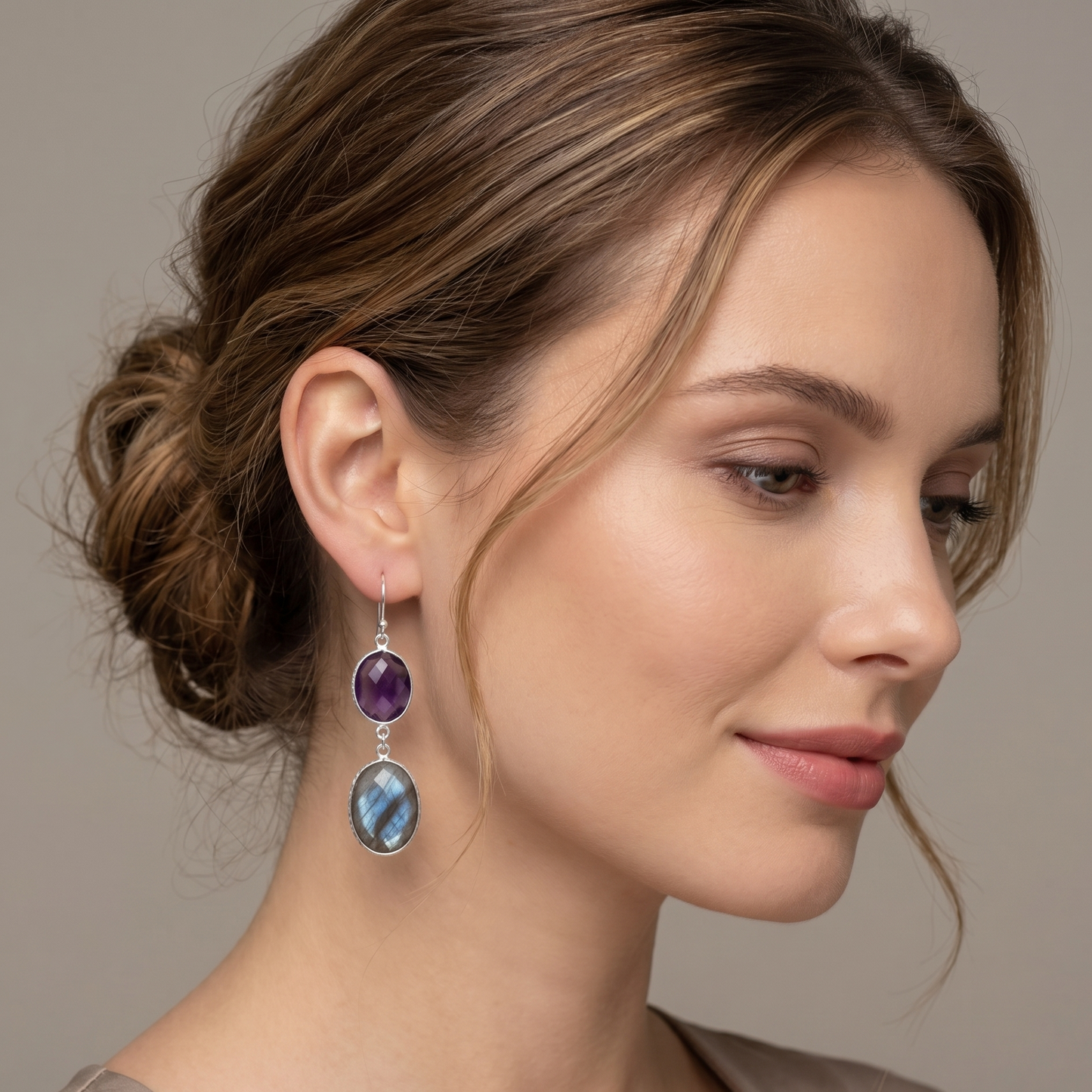 Woman wearing a pair of earrings with purple and blue gemstones on a neutral background