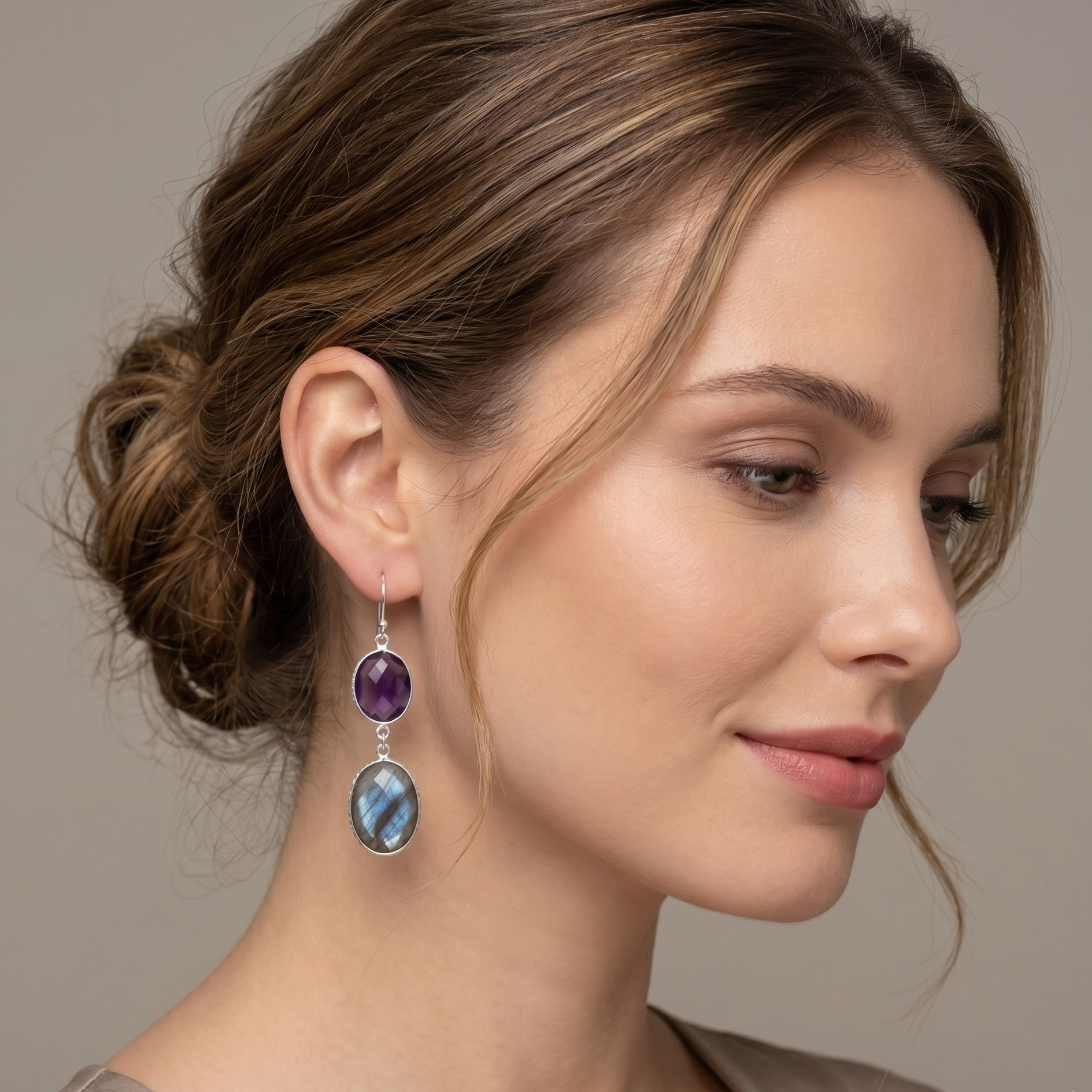 Woman wearing a pair of earrings with purple and blue gemstones on a neutral background