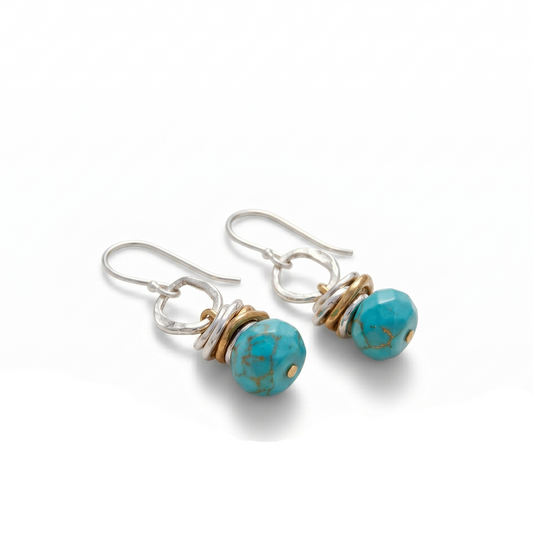 Turquoise beaded earrings on a white background with sand and driftwood.