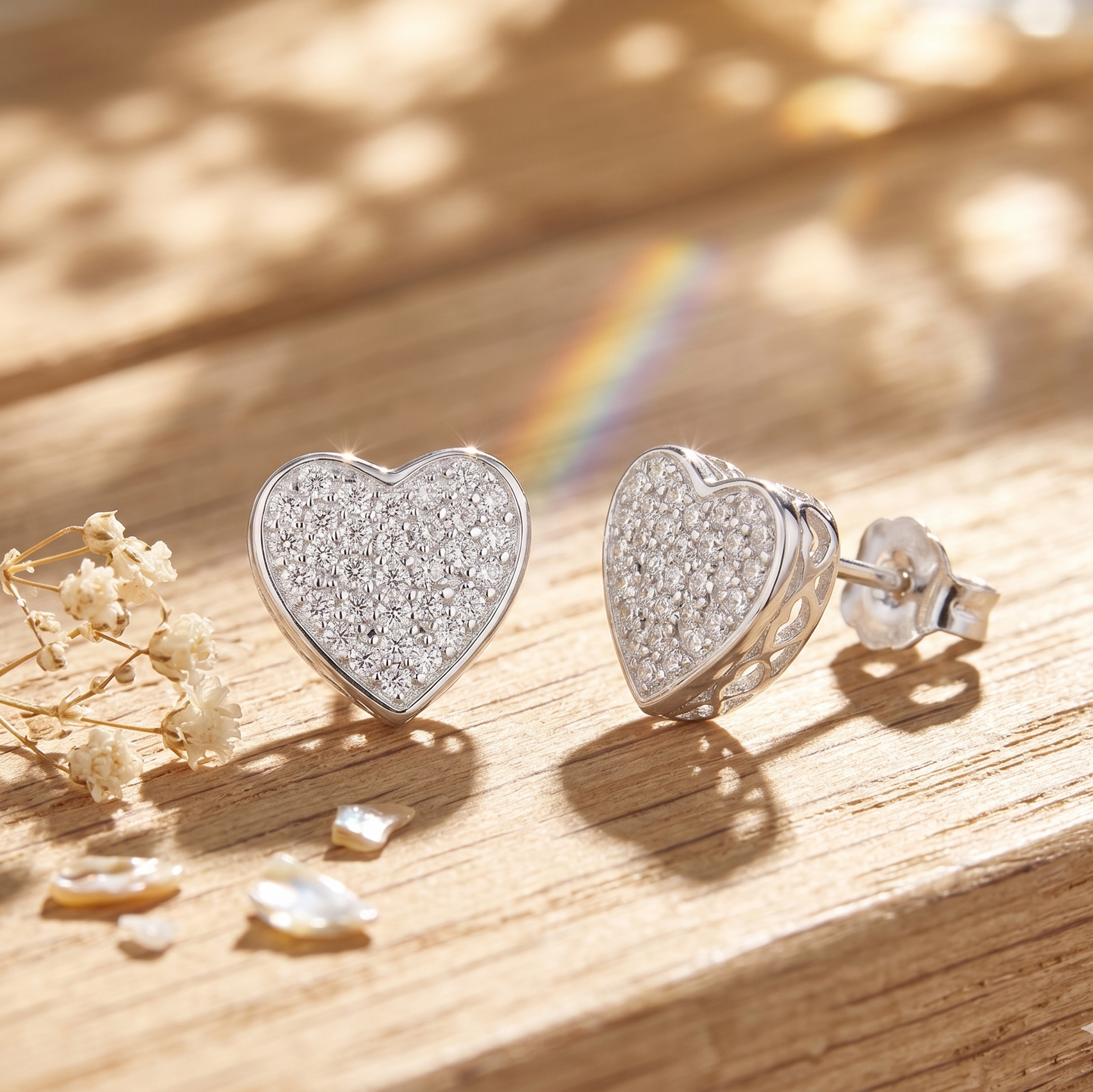 Heart-shaped silver earrings with sparkling stones on a wooden surface with a rainbow in the background.