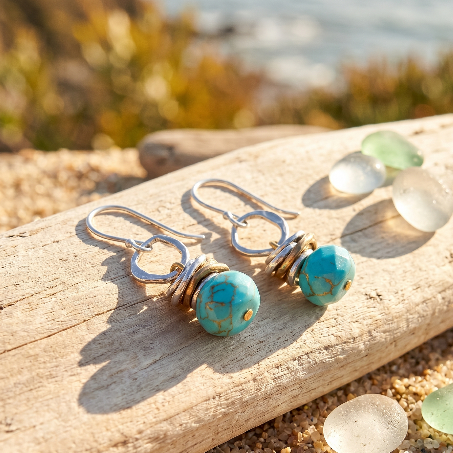 Turquoise earrings on a piece of driftwood with a beach background