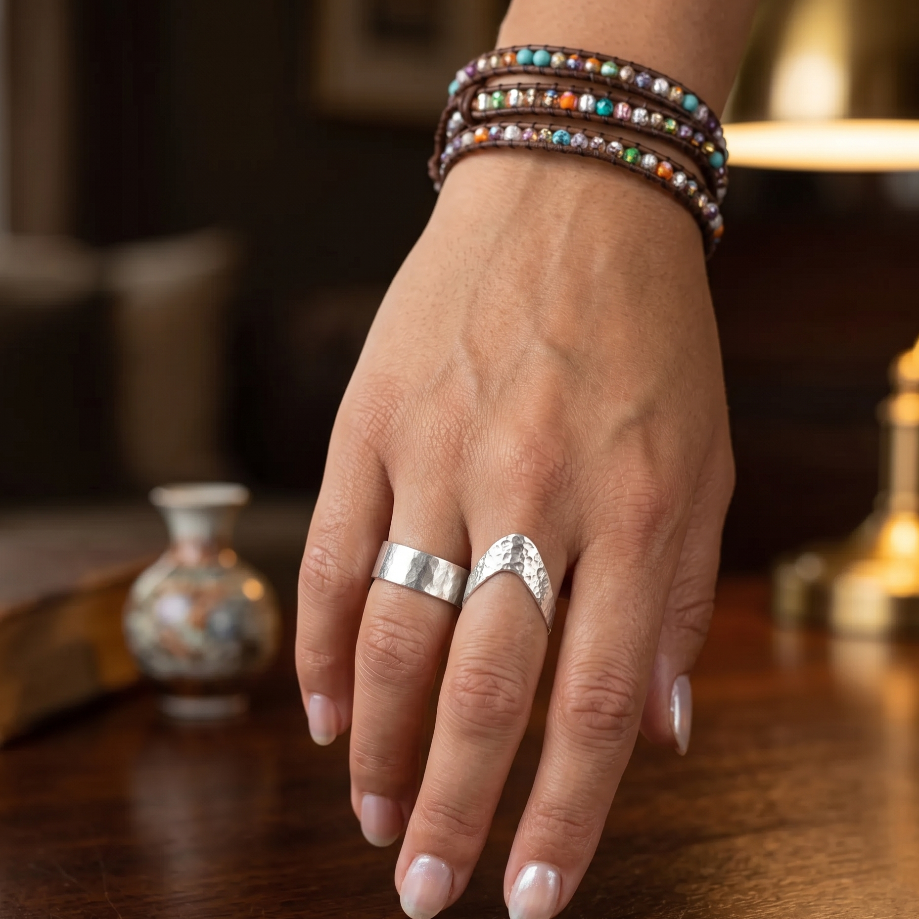 Hand wearing a silver ring and colorful bracelets on a wooden surface with a blurred background