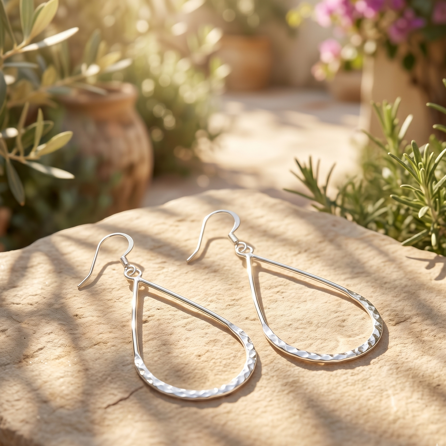 Silver teardrop earrings on a stone surface with plants in the background