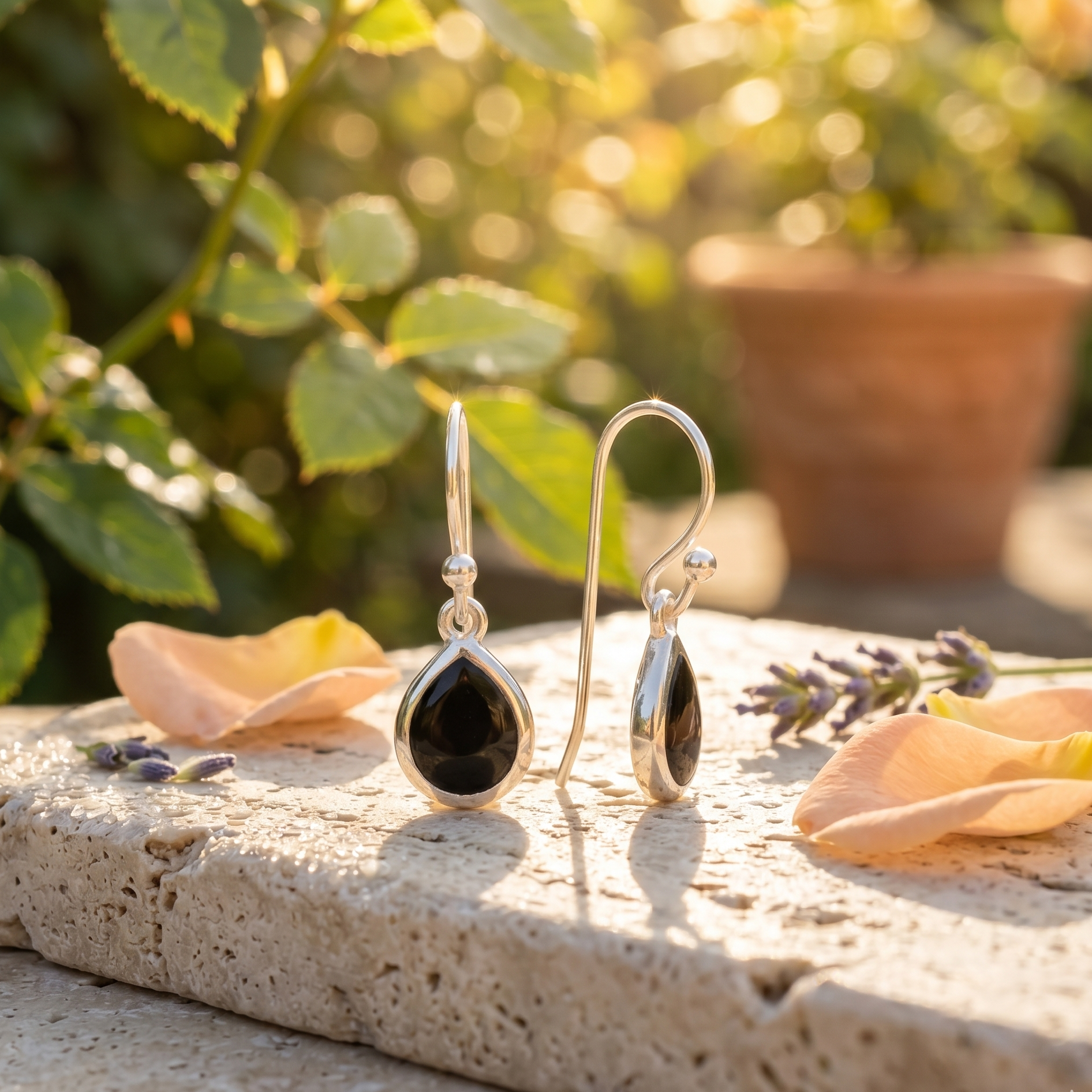 Silver earrings with black stones on a stone surface with flowers and plants in the background
