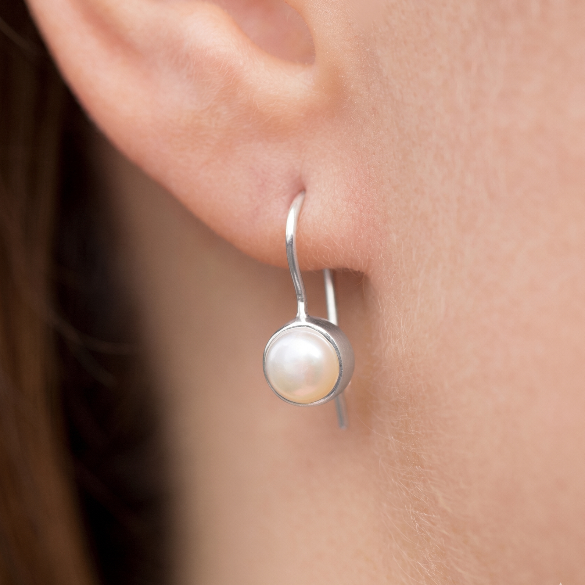 Silver earring with a pearl on an ear