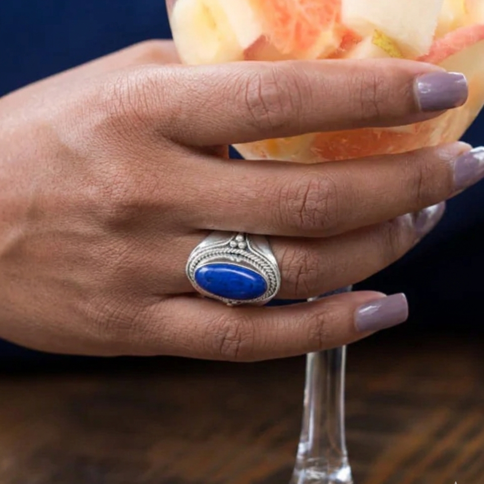 Hand holding a glass with a blue stone ring, against a dark background